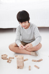 Smiling Asian cute child boy enjoying and funny with wooden blocks game in bedroom on holiday. Family activities and child educational for homeschool concept
