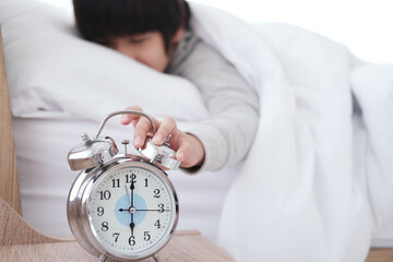 Lazy Asian boy reached out to turn off the alarm clock and wake up late with loudness on white bed before go to school in bedroom at home