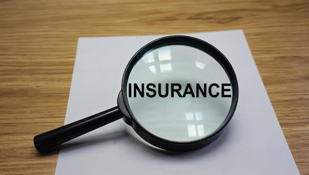 Magnifying glass focusing on word INSURANCE on paper, symbolizing scrutiny