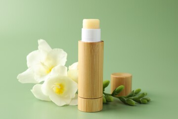 Lip balm and freesia flowers on light green background, closeup