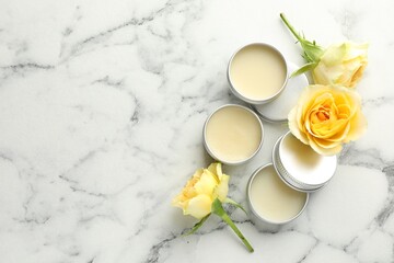 Moisturizing lip balms and yellow roses on white marble table, flat lay. Space for text