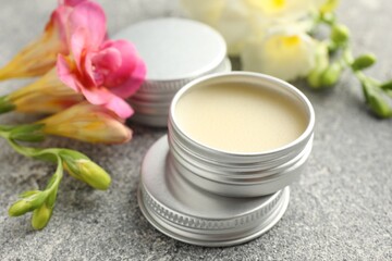 Moisturizing lip balms and beautiful flowers on grey textured table, closeup