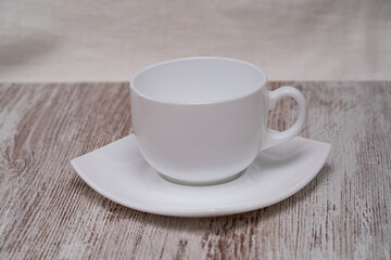 A minimalistic white cup and saucer are elegantly placed on a textured wooden surface, highlighting simplicity and sophistication in design.