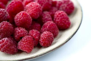 A close-up view of vibrant, fresh raspberries piled on a textured plate, showcasing their rich color and natural texture, perfect for a healthy treat.
