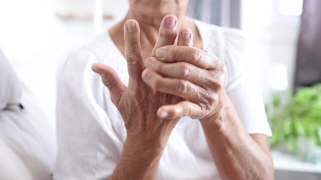 Elderly woman massaging her hand and fingers suffering chronic joint pain from Rheumatoid Arthritis, Osteoarthritis, or Gout