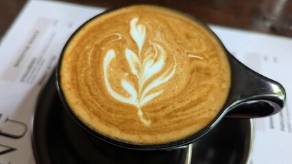 A golden flat white coffee in a black cup on a food and drinks menu at local cafe