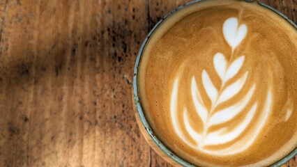 Closeup top down view of golden flat white coffee with latte art placed on a grainy rustic wooden table