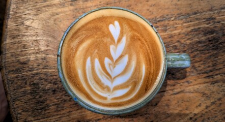 Birds eye view of flat white coffee with golden frothy milk on a rustic wooden tabletop at local cafe