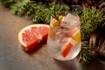 Cocktail: gin and tonic with ice, grapefruit, and rosemary on a rustic background.