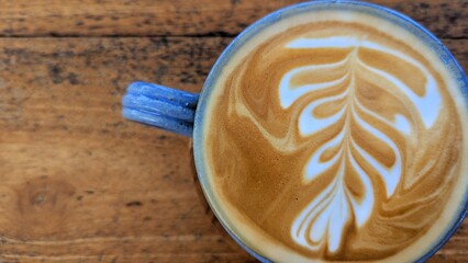 Top down view of delicious golden flat white coffee in a blue cup with latte art on a rustic wooden table top