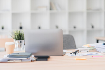 Asian businesswoman in red sweater stretches her arms while sitting at desk with laptop and stacked documents, expressing relaxation.