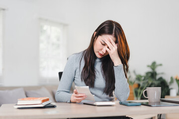 Confident Asian businesswoman smiling while working on laptop in modern home office setting.