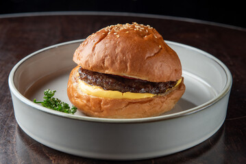 A delicious cheeseburger with a sesame seed bun and melted cheese, served on a simple white plate. The burger features a juicy beef patty and a fresh garnish.