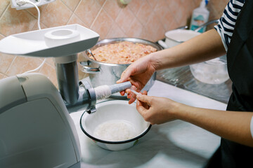 Housewife puts an intestine on a sausage attachment on an electric meat grinder