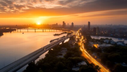 Fototapeta premium Golden sunrise illuminates a city skyline, reflecting on a river with a bridge and highway traffic