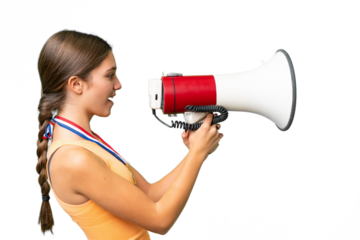 Teenager caucasian girl with medals over isolated background shouting through a megaphone