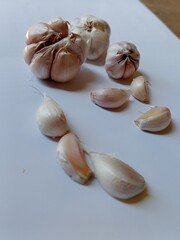 a few cloves of garlic scattered over a white surface. There are several cloves of garlic that are still whole and several cloves that have been peeled, showing the typical texture and color of garlic