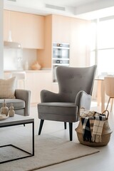 Elegant grey armchair standing near coffee table with home decor and plaid in basket. Light and modern space in an urban apartment. New furniture in living room