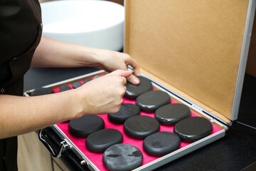 Massage Therapist's Hands Applying Oil on Basalt Stones for Relaxing Spa Treatment.