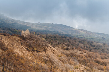 Rolling Crimea landscape with barren hills under soft, overcast sky. Earthy tones dominate, creating tranquil yet rugged scenery. Low clouds add atmosphere, enhancing quietude