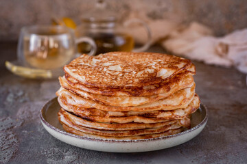 A stack of thin large pancakes on a plate on a gray background. A stack of thin pancakes for...