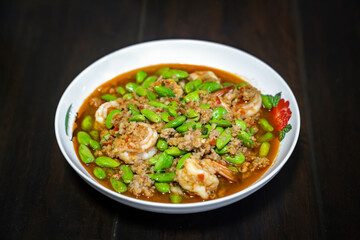 Thai Stir-Fried Stink Beans with Shrimps and spicy shrimp paste sauce in white dish bowl on dark wood table. Clipping Path.