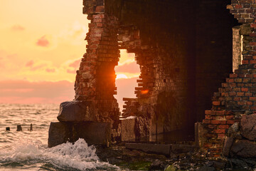 Weathered brick structure by sea at sunset evokes history and change. Waves crash against ancient...