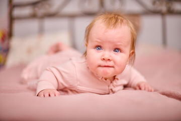 Baby girl, blonde, blue eyes, lies on soft pink bedspread, curious expression, warm lighting, cozy...