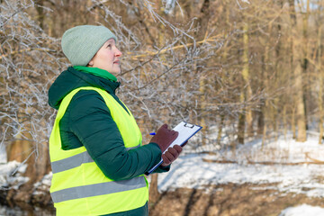 Female ecologist inspects trees. Eco volunteer. Forestry engineer works in winter. Inspector...