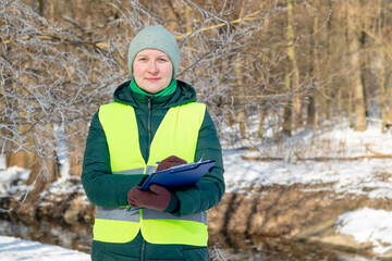 Portrait European woman with a tablet checks trees in the forest after a snowfall. Female ecologist...