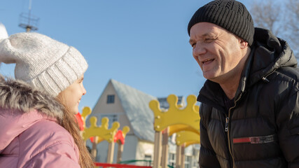 Grandfather playing with her granddaughter on the playground in the park in winter