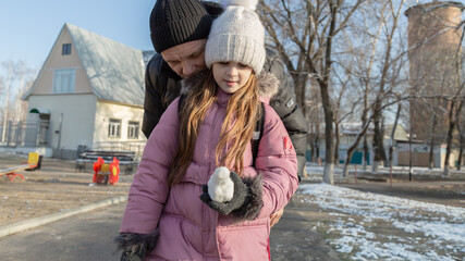 Grandfather walks with his granddaughter after school in the park in winter