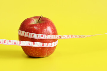 Measuring tape and red ripe apple on yellow background with copy space for text. Healthy eating and weight loss concept. Composition with white measuring tape and apple. Diet. Healthy lifestyle