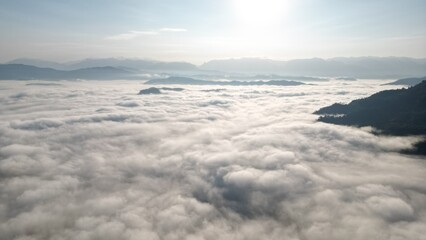 view of towering mountains enveloped in a sea of mist, with the soft glow of the morning sun casting a warm and peaceful light across the landscape. The mist creates an ethereal atmosphere, enhancing 