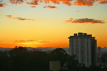 Golden sky in summer sunrise, city buikdings on shadow. Dawn with reddish clouds in the sky. Sun rising over the horizon, yellow reflections in the sky.