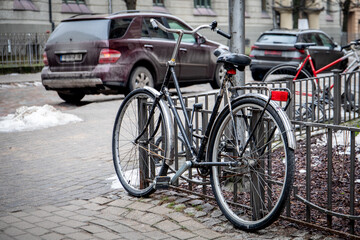 Black Bicycle Locked to a Fence in Urban Area with Cars in the Background