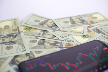 dollars and trading, the concept of trading via smartphone with a background of hundreds of US dollars, successful and failed trading, trading with a smartphone.