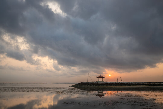 Beautiful seascape in the morning. Tropical sandy beach with breakwater and reflection of the sky in the calm water. Sanur, Bali, Indonesia