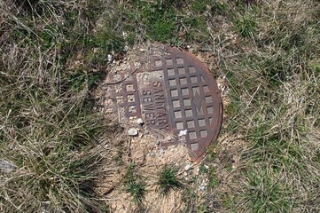 Iron lid for a sanitary sewer with grass and dirt
