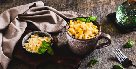 Pasta with grated cheese baked in a mug and basil leaves on the table web banner