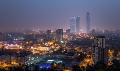 Obraz premium Cityscape at dusk with illuminated buildings, roads, and hazy sky
