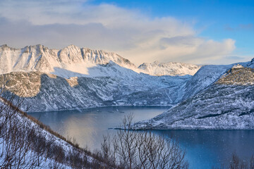Obraz premium awesome landscape above the wintry village of Fjordgard and the snowcovered steep mountains at the Oeyfjord on the Island of Senja in Northern Norway