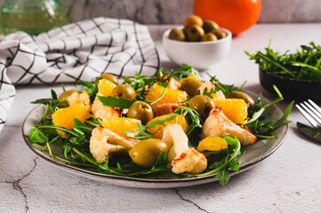 Vegetarian salad with cauliflower, orange, arugula and olives on a plate on the table