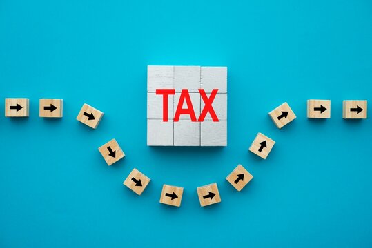 Flat lay of arrow symbol block avoid TAX word block on blue background. Tax avoidance (minimizing paying) and tax evasion (not paying) concept.