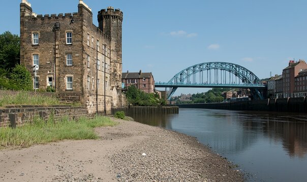 Historic castle by river with bridge, cityscape backdrop. Ideal for travel or history projects