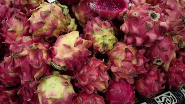 A close-up video of dragon fruits with one sliced open, revealing the bright pink pulp inside. The camera captures the vibrant colors and unique texture of these exotic fruits.