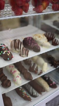 Vertical screen: Chocolate-covered strawberries with various toppings like sprinkles and drizzles of white chocolate are beautifully arranged on display.