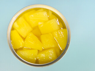 A closeup, overhead, off-centre, isolated shot of an open tin can of chopped pineapple chunks in juice.