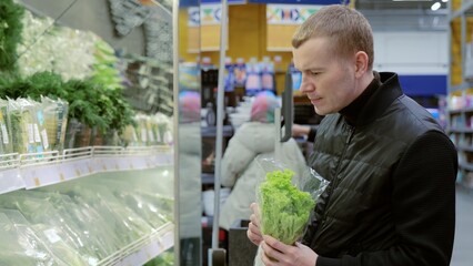 Man choosing greens in supermarket, shelf with greens. Man making healthy food choices in a supermarket, carefully selecting fresh produce among a variety of options