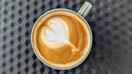 Top down view of heart shaped latte art in golden flat white coffee drink on textured matte black mat